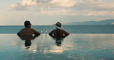 Couple relaxing together in infinity pool with sea view and drinking champagn Stock Footage 163666213