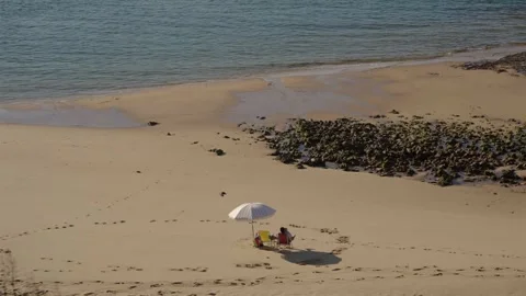 Couple relaxing under a beach umbrella on an empty sandy beach, Portugal Stock Footage 346374407