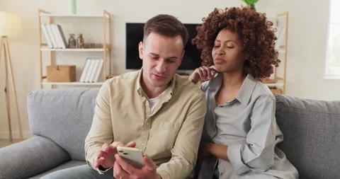Couple reviewing smartphone content on sofa and discussing plans at home Stock Footage 337929383