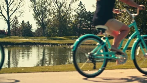 Couple Rides Bikes on Path in front of Geese on a lake out of focus 스톡 동영상 280705385