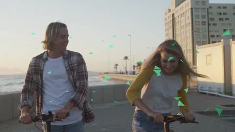 Couple riding scooters approaching frame, green animated triangles overlaying Stock Footage 334743647