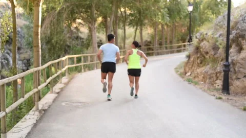 Couple run away with their backs to camera along the road surrounded by nature Stock Footage 144120056