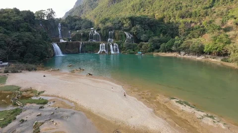 Couple Run Down the Beach with Ban Gioc Waterfall in Vietnam Behind Drone Video Stock Footage 125497707