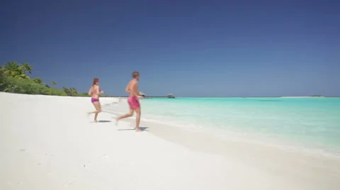 Couple running across beach into waves Stock Footage 1009061