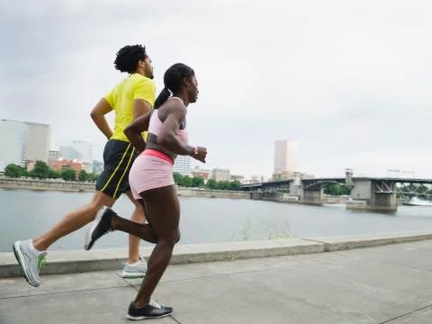 Couple running along urban waterfront Stock Photos