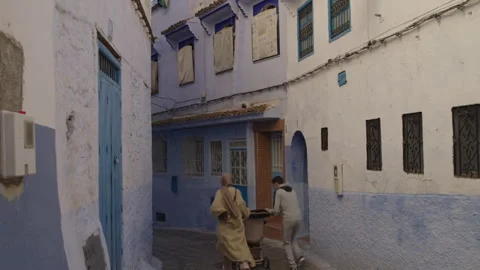 Couple running with baby stroller on empty street of blue city of Chefchaouen Stock Footage 265497632