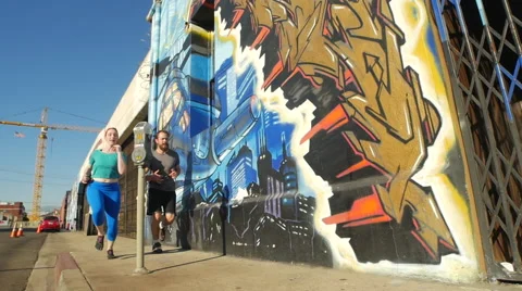 A couple running by a graffiti covered wall in an urban environment. Stock Footage 67981239