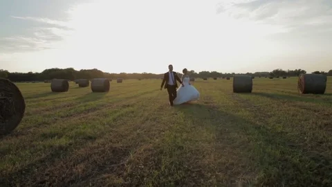 Couple running on meadow at sunset. The bride and groom holding hands. Stock Footage 74714478