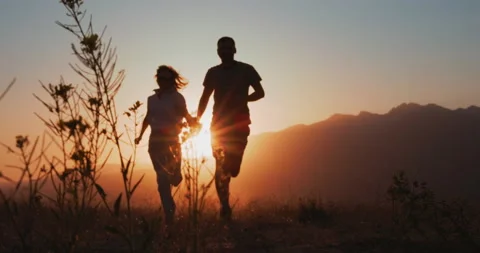 Couple running in a mountain field at sunset Stock Footage 229897025