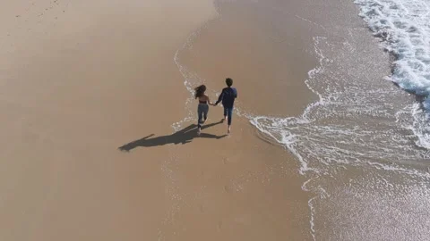 Couple Running In The Shore Of Beach With Waves. - aerial follow shot Stock Footage 310954827