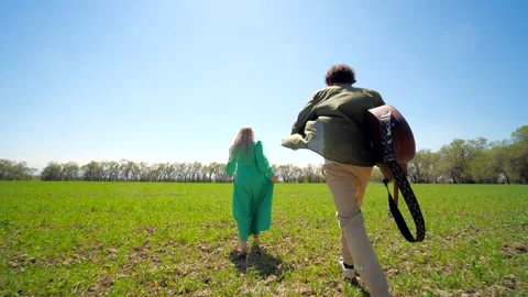 Couple running through green field in spring, man with guitar, wide-angle shot Video stock 301339070