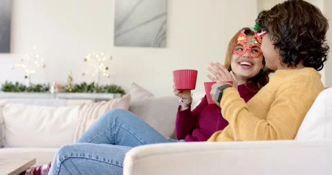 Couple settling on couch at home celebrating holiday by lifting red mugs, Stock Footage 340972501