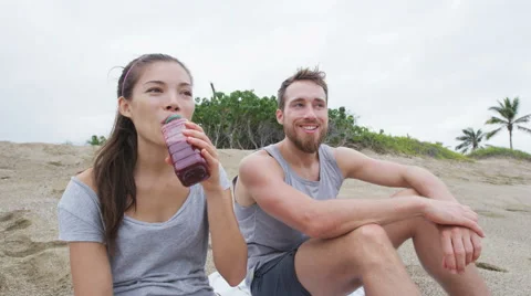Couple sharing beet juice on beach after exercise - people in healthy lifestyle Stock Footage 61746158