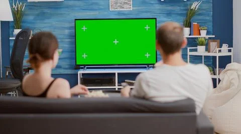 Couple sharing a bowl of popcorn while watching tv and switching channels Stock Photos