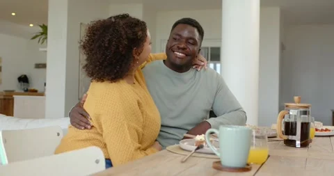 Couple sharing breakfast at wooden table, woman leaning in and cupping man's Stock Footage 341953077