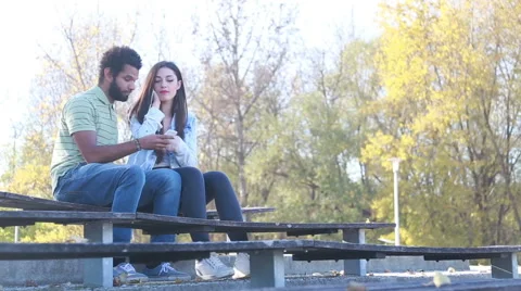 Couple sharing earphones while listening to music at park Stock Footage 59555238