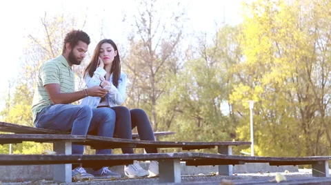 Couple sharing earphones while listening to music at park Stock Footage 59555247