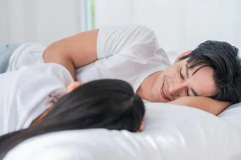 Couple sharing a joyful moment while lying together on a bed in a cozy room.. Stock Photos