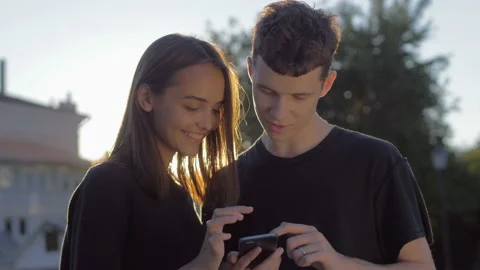 Couple sharing media in a smart phone sitting in a bench in a park with Stock Footage 93551853