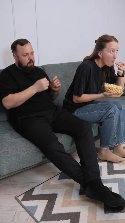 Couple sharing popcorn while watching movie on sofa Vidéo 317444593