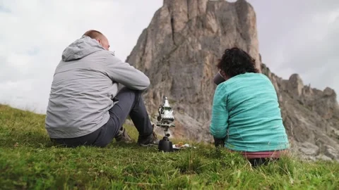 Couple sharing tea on grassy hill with rocky Dolomites cliffs in the background Vidéo 318949723