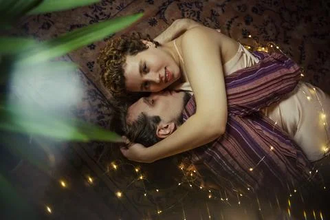 Couple sharing a tender moment while lying on a cozy carpet surrounded by soft Stock Photos