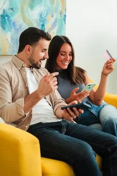 Couple shopping together on couch using mobile device and card for online Stock Photos