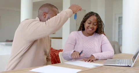 Couple signing papers at table man holding blue keys woman taking them hugging Stock Footage 339495772