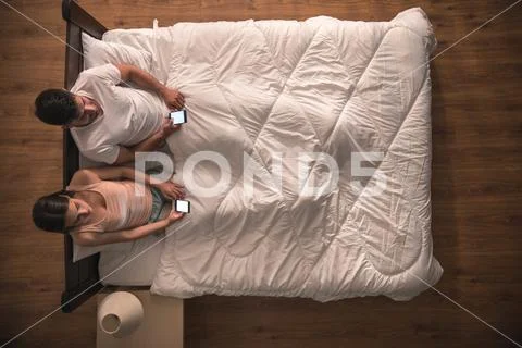 The couple sit on the bed and phone. view from above Stock Photos