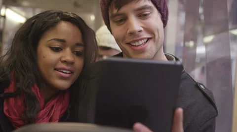 A couple sit on a bus and have fun talking and looking at their tablet Stock Footage 34017529