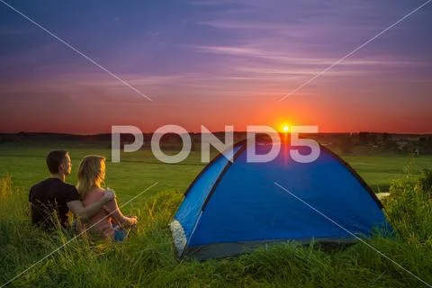 The couple sit near camping tent by sunset (sunrise) background. Wide anlge Stock Photos