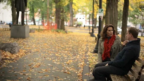 A couple sit at a park bench and talk to each other on a nice fall day Stock Footage 98380838