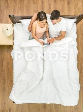 The couple sit with a phone on the bed. View from above Stock Photos