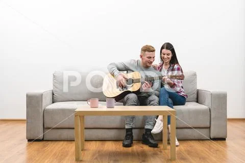 The couple sit on the sofa and play the guitar on the white wall background Stock Photos