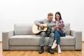 The couple sit on the sofa and play the guitar on the white wall background Photo