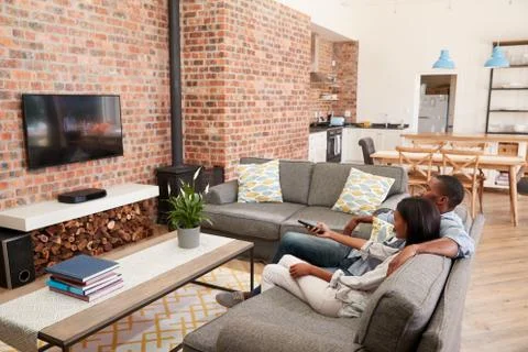 Couple Sit On Sofa In Open Plan Lounge Watching Television Fotos de archivo