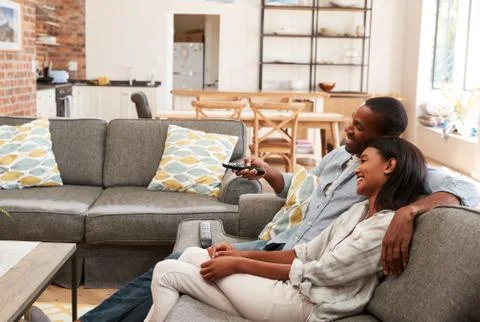 Couple Sit On Sofa In Open Plan Lounge Watching Television Fotos de archivo