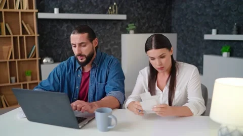 Couple sit at a table in front of a laptop and sort out bills checks taxes notes Stock Footage 236588402