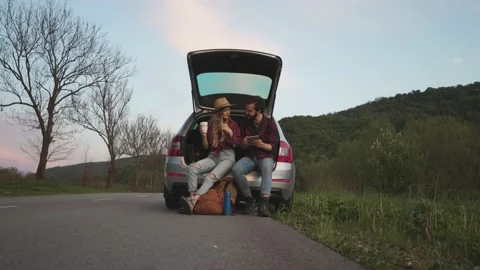 Couple sit on the trunk of car and wonder at photo on tablet Stock Footage 131458967