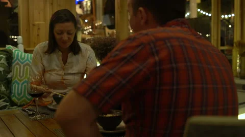 The couple sits and eats at the restaurant. A man pours a woman a glass of red Stock Footage 92270082