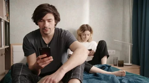 A couple sits in bed, the guy shows his phone to a woman and tells something Stock-Footage 197364258