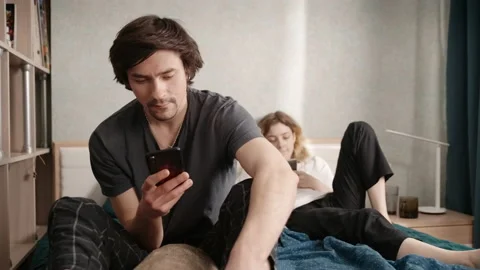A couple sits in bed, then the guy shows his phone and they smile Vidéo 197364837