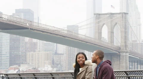 A couple sits on a bench and talks while in front of the Brooklyn Bridge Stock Footage 45760658