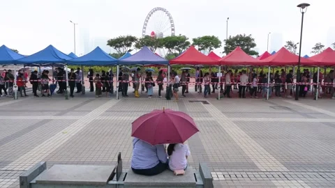 A couple sits on a bench in front of a queue of residents to receive PCR Stock Footage 210214736