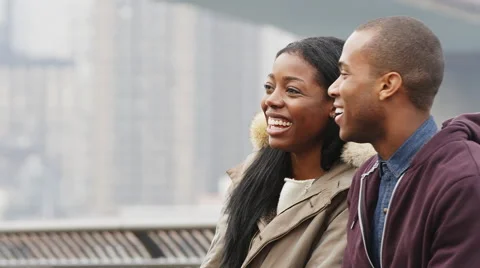 A couple sits on a bench in a park in front of the brooklyn bridge on an Stock Footage 45759597