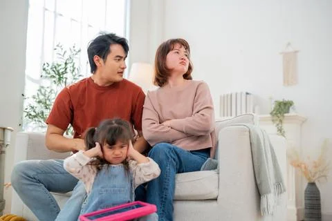 Couple sits on couch while child covers ears during family discussion in li.. Foto stock
