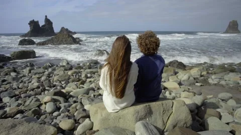 The couple sits facing the ocean and admires the rocks Stock Footage 219349895