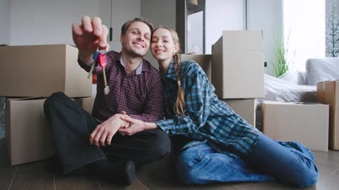 A couple sits on the floor surrounded by cardboard boxes in their new home Stock Footage 346226203