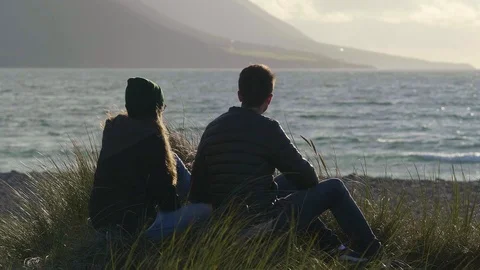 Couple sits at the oceanfront while watching the sunset Stock Footage 95559778