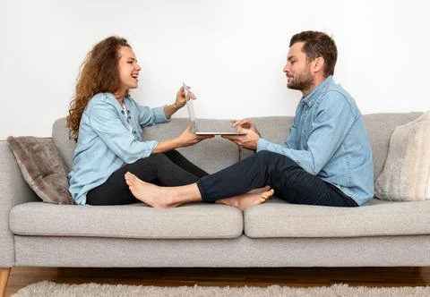Couple sits on sofa and using one laptop together. Booking online. Internet s Stock Photos
